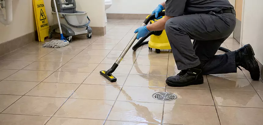 Technician using a wet vacuum to remove water from a flooded bathroom tile floor.